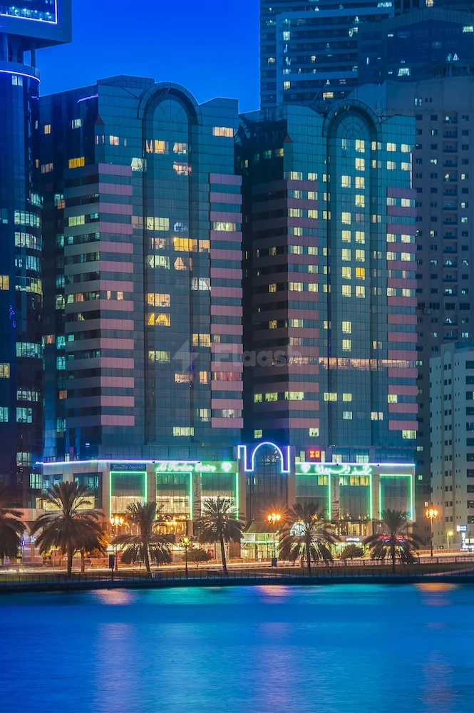 Modern hotel facade at Golden Tulip Sharjah, Sharjah, illuminated with neon signage and framed by palm trees along