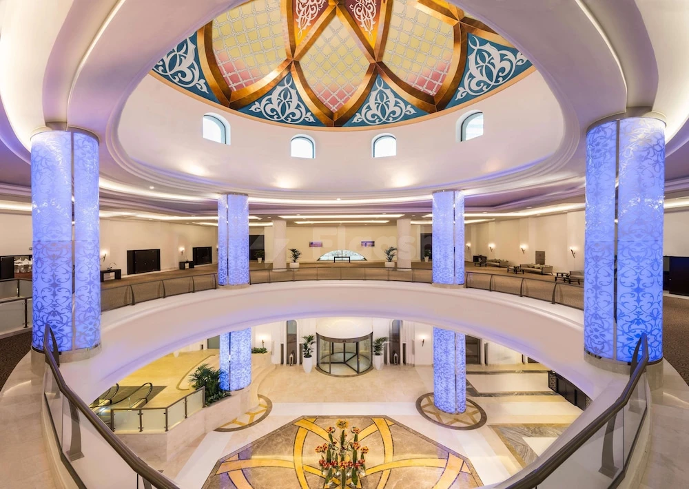 Grand atrium at Bahi Ajman Palace Hotel, Ajman, featuring illuminated blue patterned columns and ornate domed ceiling