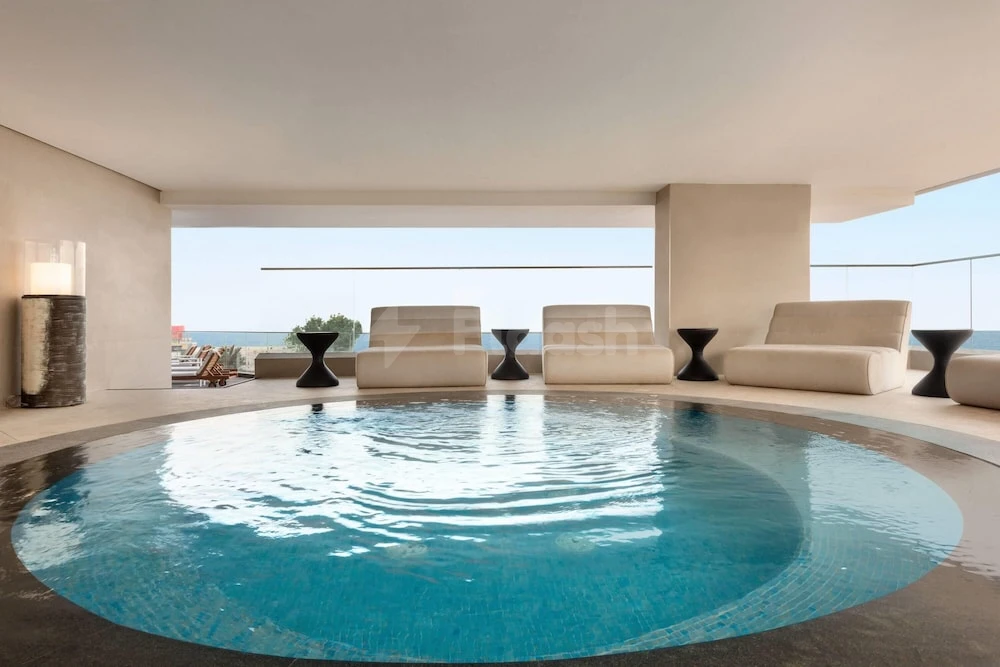 Indoor infinity pool at Wyndham Garden Ajman Corniche, Ajman, with lounge chairs and glass railing overlooking sea