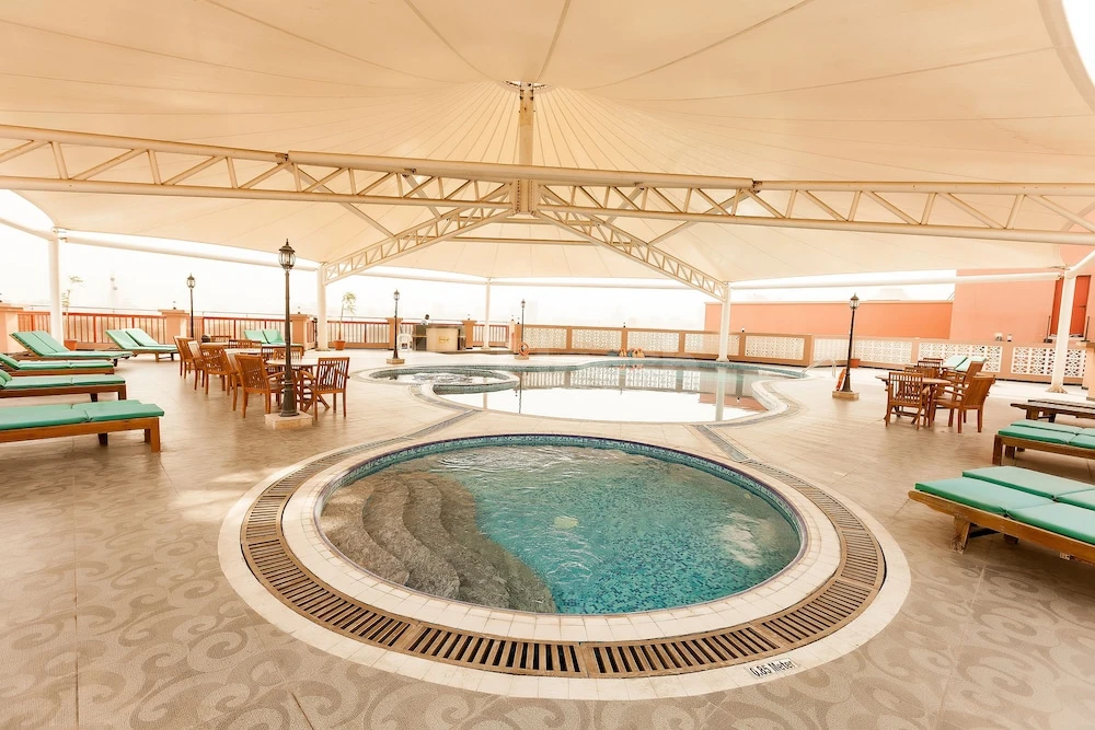Covered pool area at Red Castle Hotel, Sharjah, featuring circular jacuzzis and wooden lounge chairs under a large