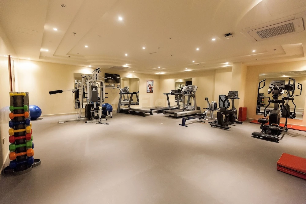 Fitness center at Red Castle Hotel, Sharjah, featuring treadmills and colorful dumbbell rack under warm ceiling lights