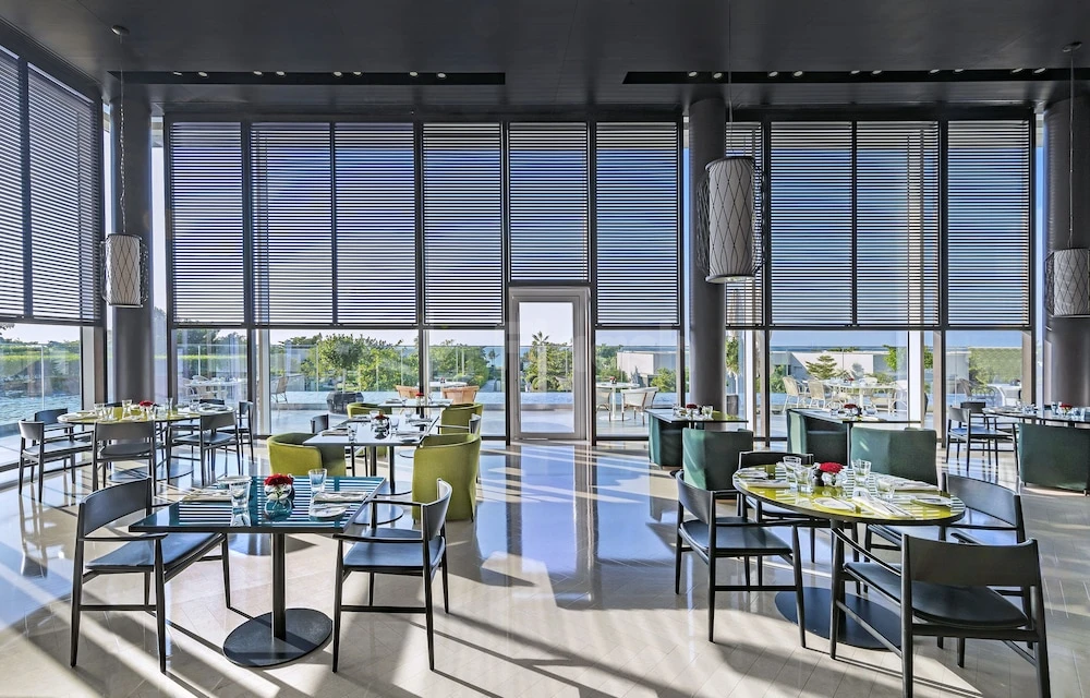 Dining room at Al Zorah Beach Resort, Ajman, with floor-to-ceiling windows and modern pendant lights above tables