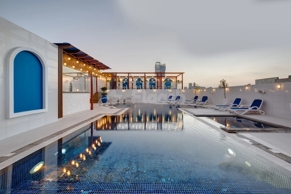 Rooftop pool at Donatello Hotel Dubai, Dubai, with blue mosaic tiles and string lights over arched wall openings
