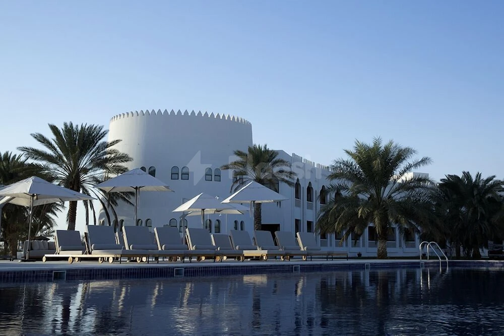 Poolside lounge area at Liwa Hotel, Abu Dhabi, with white umbrellas and palm trees lining the edge