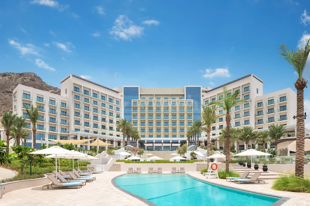 Outdoor pool area at Address Beach Resort Fujairah, Fujairah, with lounge chairs and palm trees under blue sky