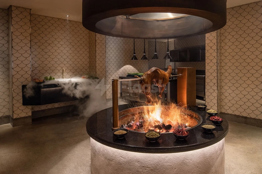 Dining room at The Chedi Al Bait, Sharjah, featuring central fire pit with roasted lamb and scalloped tile