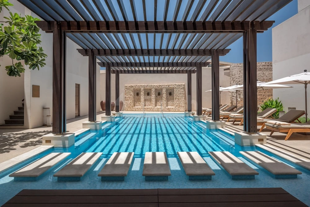 Poolside lounge at The Chedi Al Bait, Sharjah, featuring sunken stone benches shaded by wooden pergolas