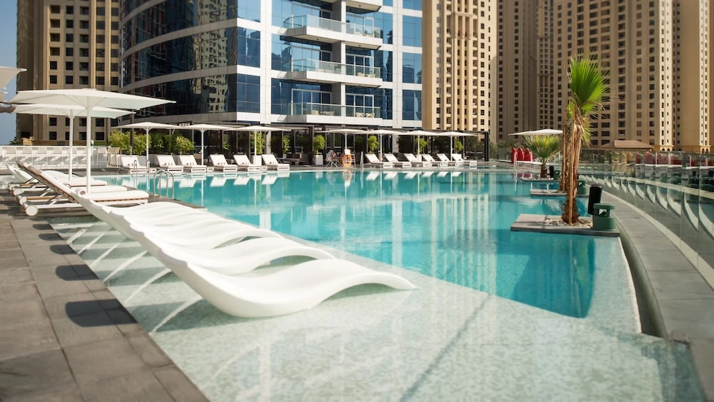 Outdoor pool at InterContinental Dubai Marina, Dubai, lined with white lounge chairs and modern umbrellas