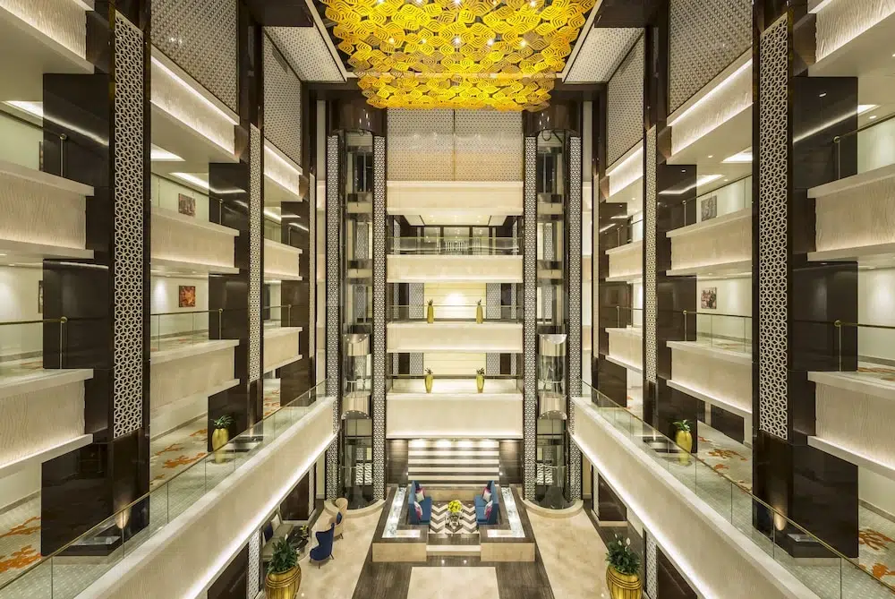 Grand atrium at Radisson Blu Hotel Ajman, Ajman, featuring golden ceiling sculpture and glass-walled elevators