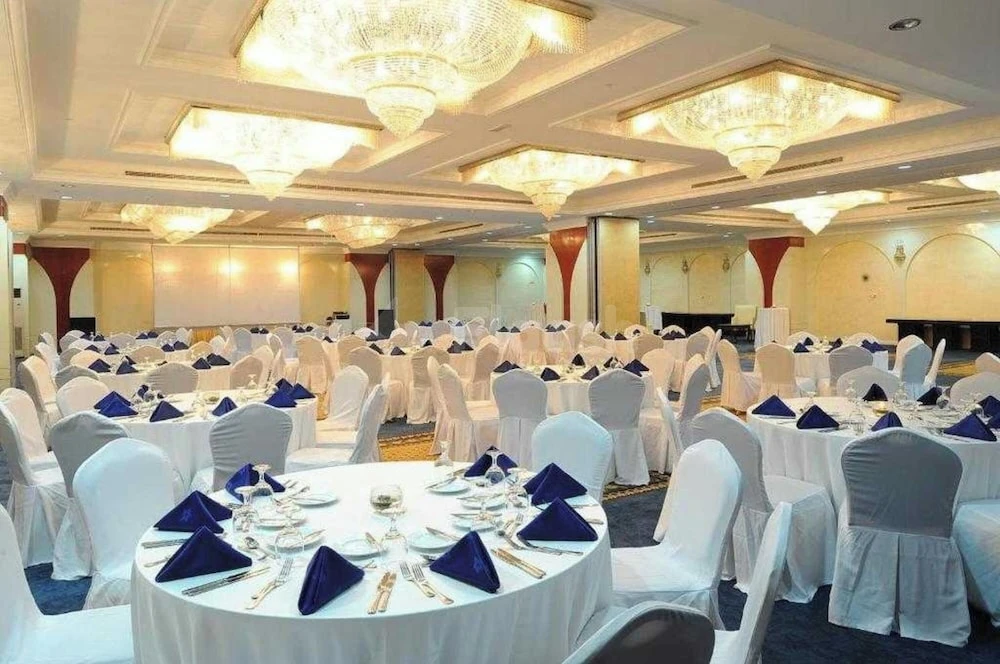 Banquet hall at Hotel Holiday International, Sharjah, with white-draped tables and blue napkins under crystal chandeliers