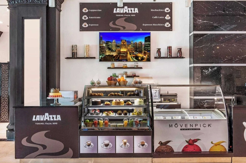 Coffee bar at Hotel Holiday International, Sharjah, with Lavazza branding and glass pastry display