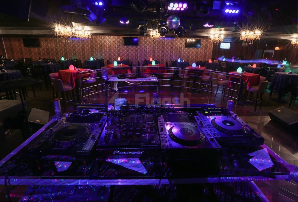 DJ booth at Ramee Royal Hotel, Dubai, with Pioneer turntables under purple lights and crystal chandeliers above tables