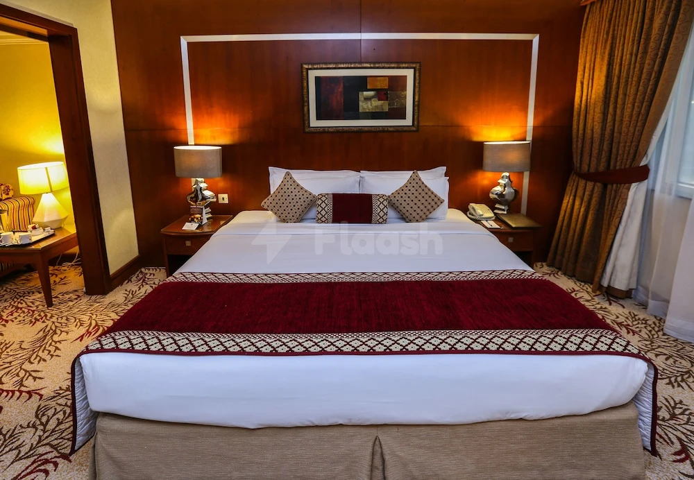 Guest room at Ramee Royal Hotel, Dubai, featuring wooden headboard and red patterned bed runner
