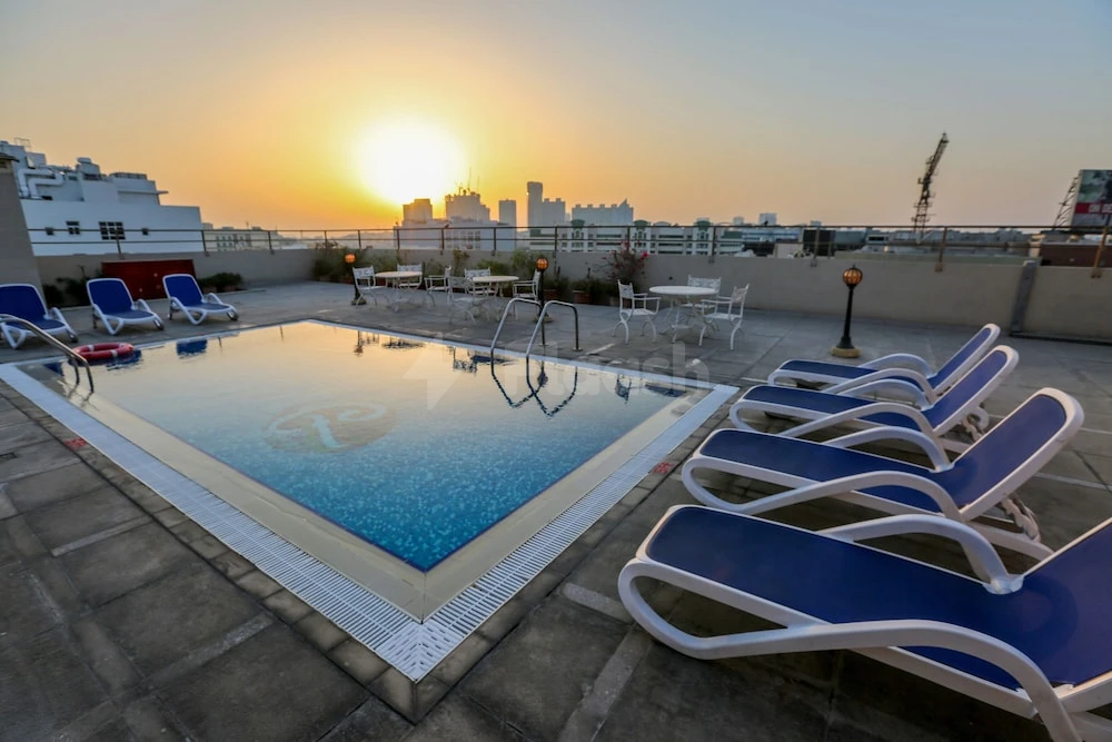 Rooftop pool at Ramee Royal Hotel, Dubai, with blue lounge chairs and city skyline at sunset