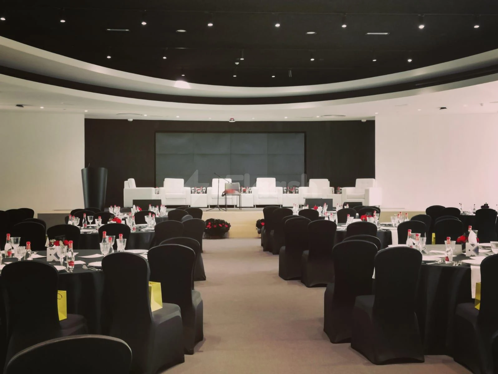 Banquet hall at YourSpace, trúe, Aljada, Sharja, with red floral centerpieces and black white chairs on stage