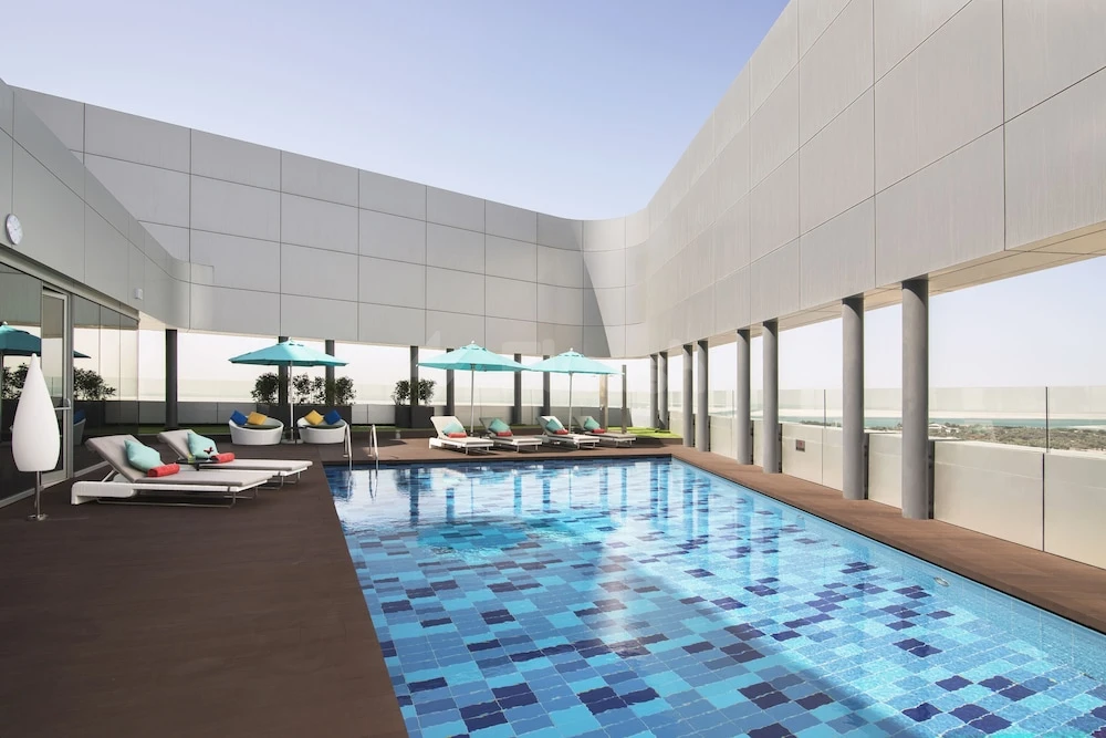 Rooftop pool at Pearl Rotana Capital Centre, Abu Dhabi, featuring blue mosaic tiles and lounge chairs under turquoise