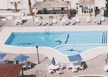 Outdoor swimming pool at Ajman Beach Hotel, Ajman, with lounge chairs and blue umbrellas surrounding clear water