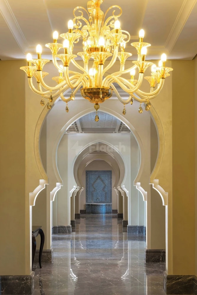 Grand hallway at Ajman Saray, Ajman, featuring arched doorways and ornate chandeliers over polished marble floors