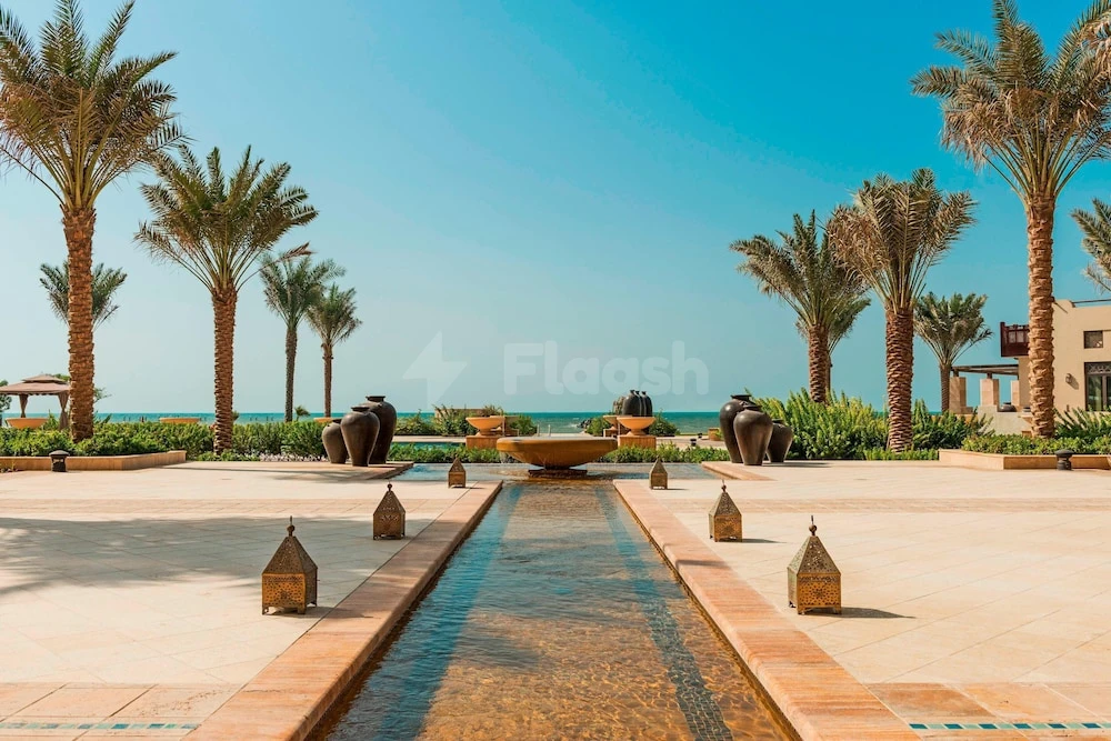 Water feature courtyard at Ajman Saray, Ajman, lined with palm trees and lanterns under clear sky