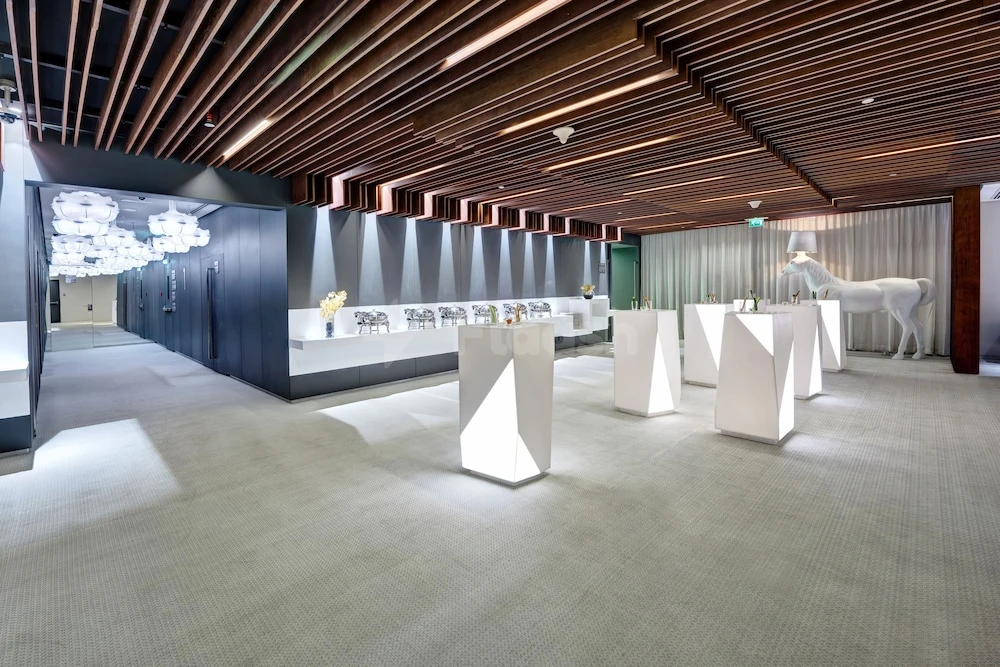 Exhibition space at The Act Hotel, Sharjah, featuring geometric white pedestals and a glowing horse sculpture under wooden