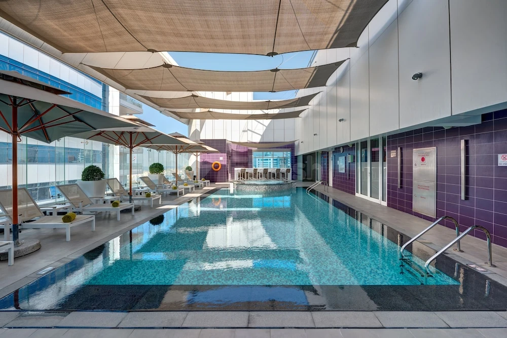 Indoor pool area at The Act Hotel, Sharjah, with purple tiled walls and shaded lounge chairs