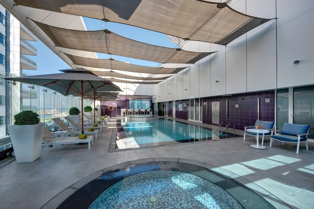 Outdoor pool area at The Act Hotel, Sharjah, featuring sunshades and mosaic-tiled circular spa