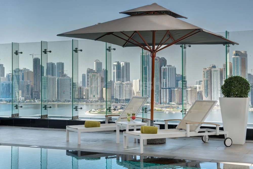 Rooftop pool at The Act Hotel, Sharjah, with lounge chairs and city skyline view through glass railings