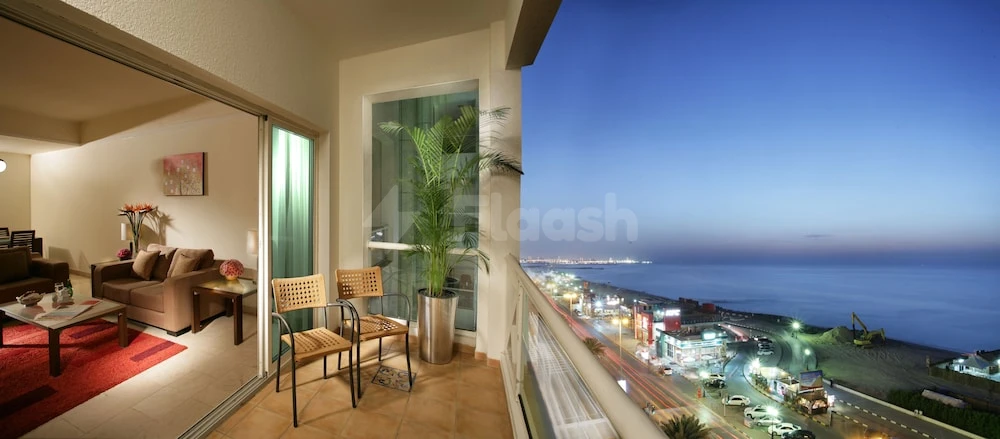 Balcony at Ramada by Wyndham Beach Hotel Ajman, Ajman, overlooks illuminated waterfront with wicker chairs and potted plant