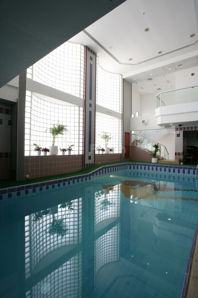 Indoor pool at Ramada by Wyndham Beach Hotel Ajman, Ajman, with grid-patterned glass walls and potted plants along