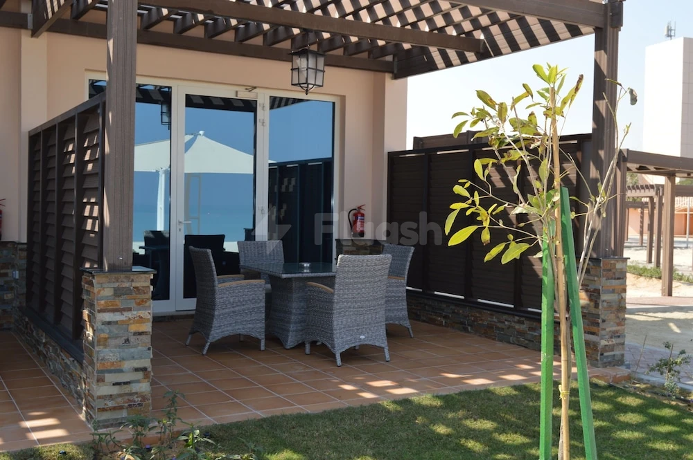 Pergola-covered patio at Danat Jebel Dhanna Resort, Abu Dhabi, features wicker furniture and stone pillars with tiled flooring