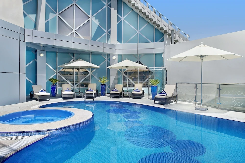 Rooftop pool at City Seasons Towers Hotel, Dubai, featuring circular mosaic tiles and white umbrellas against blue glass