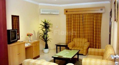 Living room at Holiday Beach Motel, Fujairah, featuring beige walls, patterned curtains, and a coffee table with potted