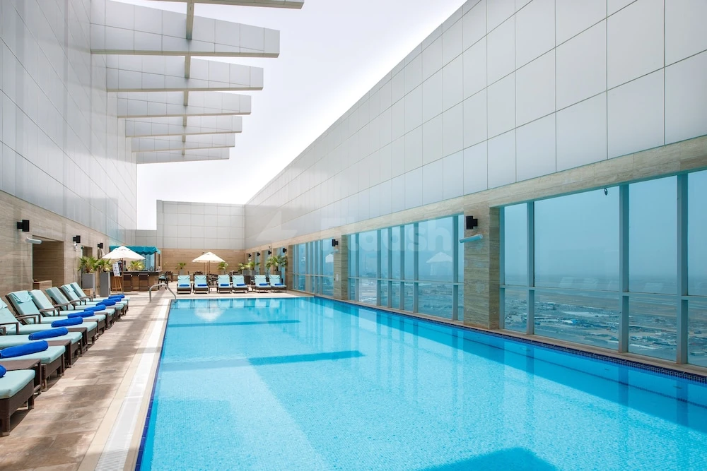 Indoor pool at Royal M Hotel Fujairah, Fujairah, featuring glass walls and lounge chairs under a modern ceiling