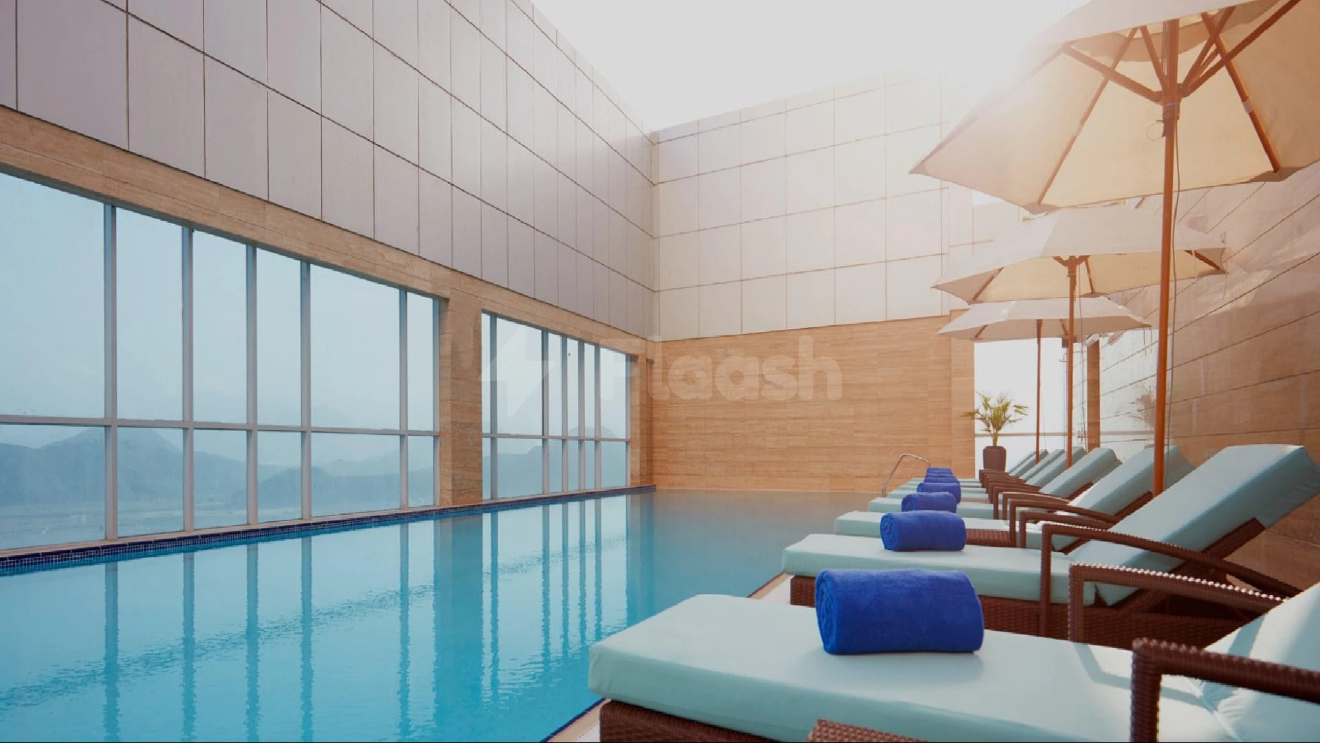 Indoor pool at Royal M Hotel Fujairah, Fujairah, with lounge chairs and blue towels neatly arranged