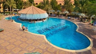 Poolside area at Bin Majid Beach Resort, Ras Al Khaimah, featuring vibrant blue water and a thatched umbrella