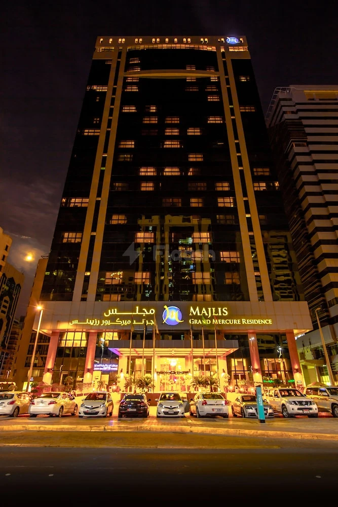 Night view of Majlis Grand Mercure Residence Abu Dhabi, illuminated facade with cars parked outside