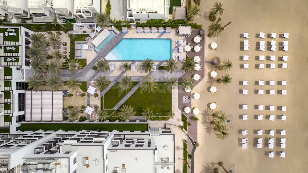 Pool deck at Palace Beach Resort Fujairah, Fujairah, lined with white umbrellas and palm trees beside turquoise water
