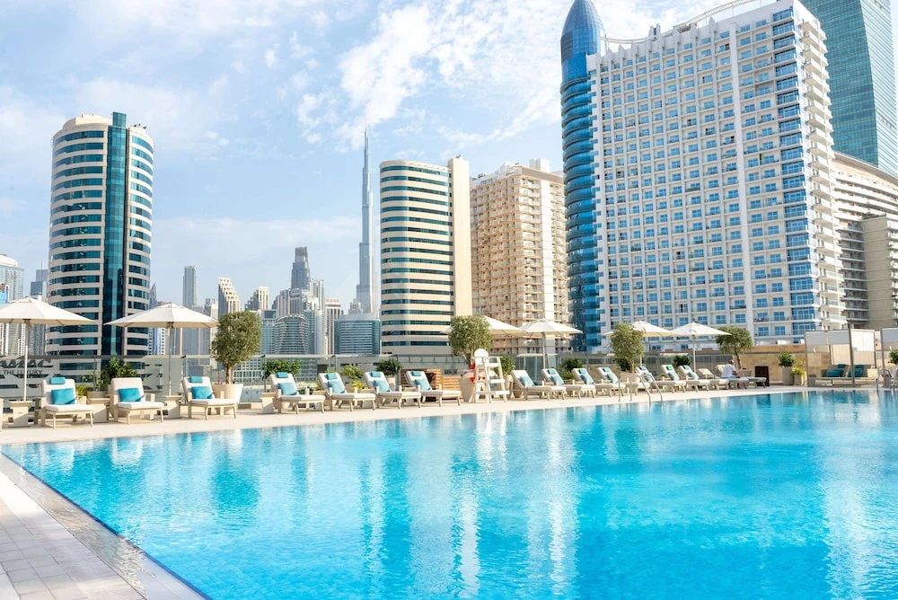Rooftop pool at The First Collection Dubai Business Bay, Dubai, lined with lounge chairs and umbrellas under modern