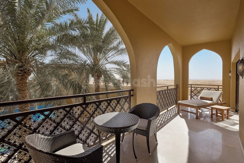 Balcony at Aldhafra Resort, Abu Dhabi, with arched openings and desert palms beyond a lattice railing