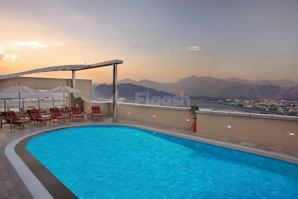 Rooftop pool at Nour Arjaan by Rotana Fujairah, overlooking mountains and sea with lounge chairs under umbrellas