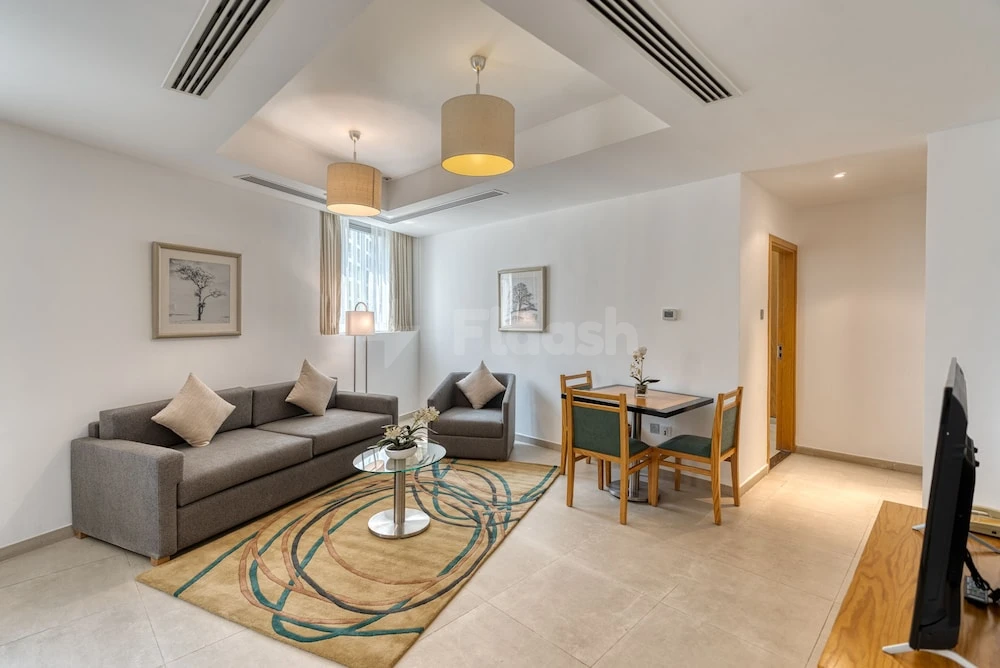 Living space at Grand Heights Dubai Hotel Apartments, Dubai, with gray sofa and circular rug under pendant lights