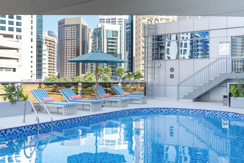 Rooftop pool at Grand Heights Dubai Hotel Apartments, Dubai, with blue-tiled deck and lounge chairs under umbrella shade