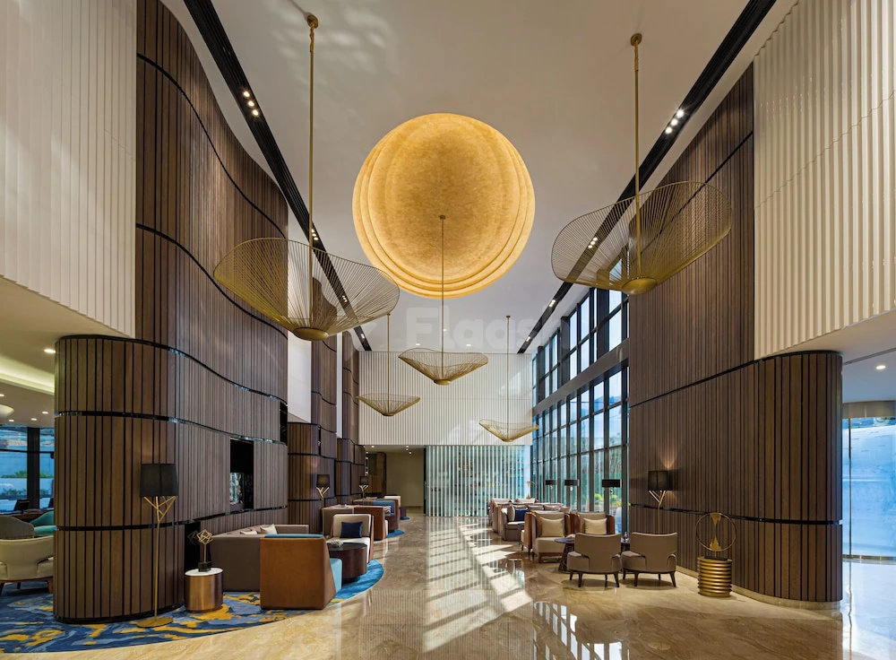 Lobby at Millennium Place Marina, Dubai, features a large circular pendant light and wood-paneled walls with tall windows