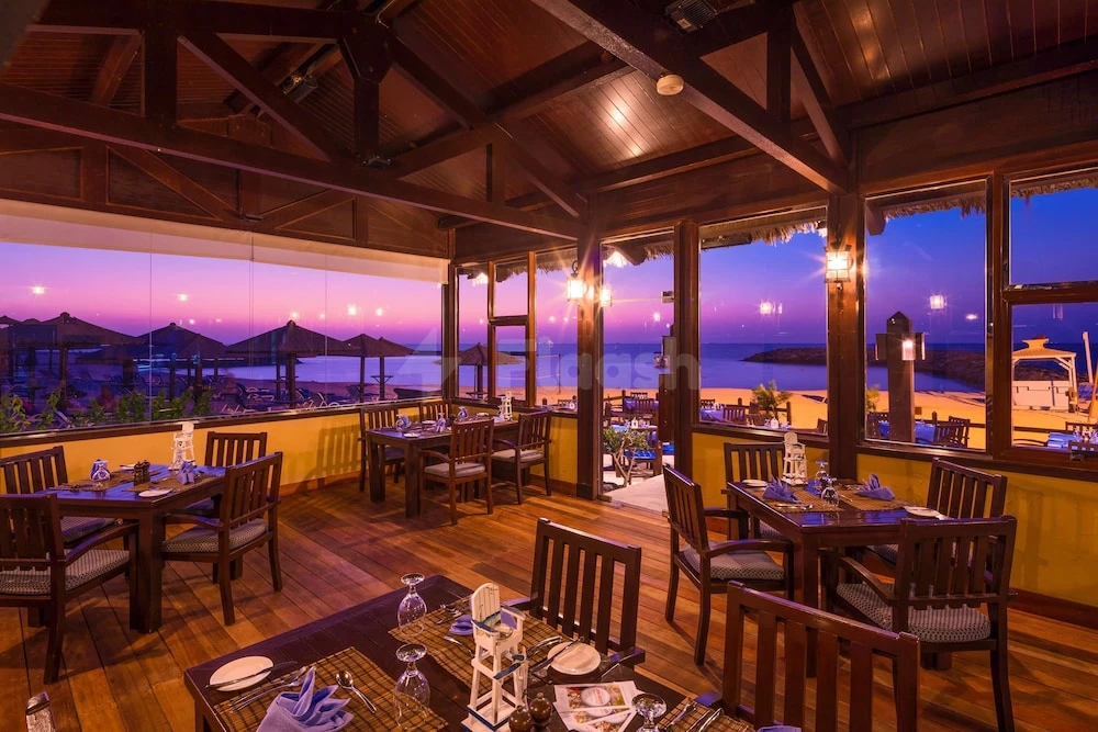 Dining room at Coral Beach Resort, Shar, with wooden beams and sunset beach views through large windows