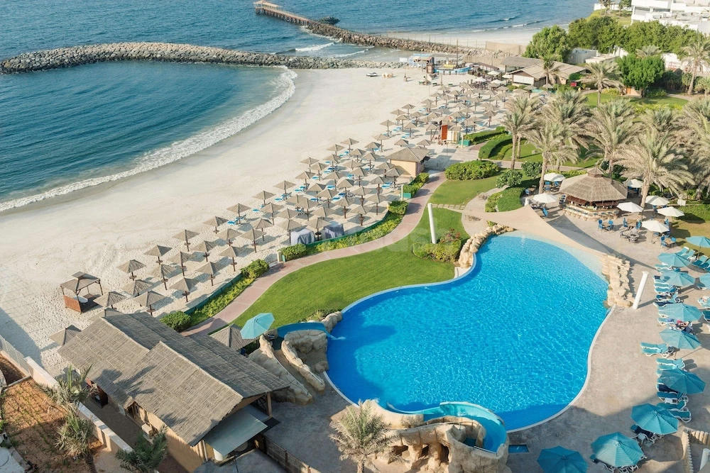 Oceanfront pool at Coral Beach Resort, Sharjah, with blue umbrellas lining the beach